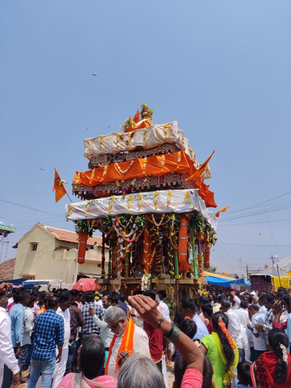 ಕೇಸರಿ ಧ್ವಜಗಳಿರುವ ಎತ್ತರದ ರಥದತ್ತ ಭಕ್ತರು ಬಾಳೆಹಣ್ಣು ಎಸೆಯುತ್ತಿರುವುದು