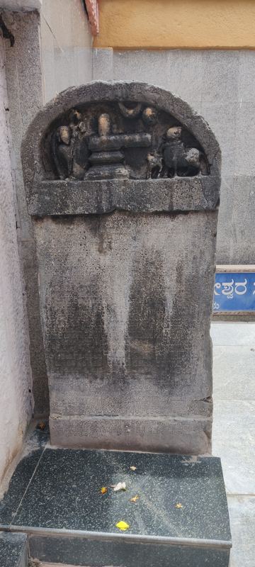 ದೇವಸ್ಥಾನದ ಆವರಣದಲ್ಲಿ ಕಪ್ಪು ಕಲ್ಲಿನ ಪೀಠದ ಮೇಲೆ ನಿಲ್ಲಿಸಿರುವ, ಕಮಾನಿನಾಕಾರದ ಮೇಲ್ಭಾಗವಿರುವ ಹೊಯ್ಸಳ ಕಾಲದ ಶಾಸನ ಕಲ್ಲು